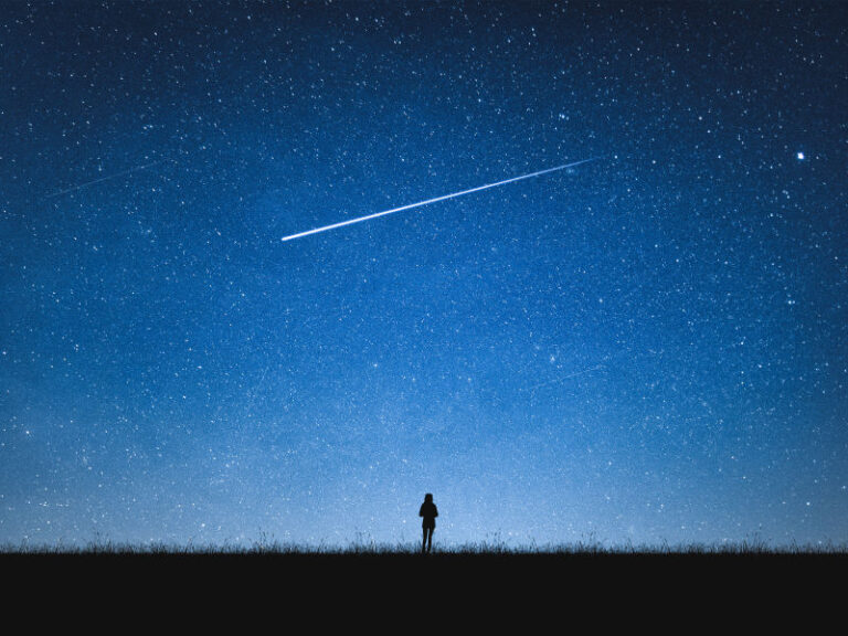 Silhouette eines Menschen vor dunklem Nachthimmel mit Sternschnuppe